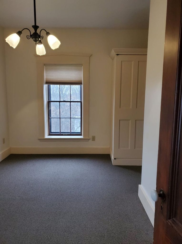 Carpeted living room with window at Adams House Apartments