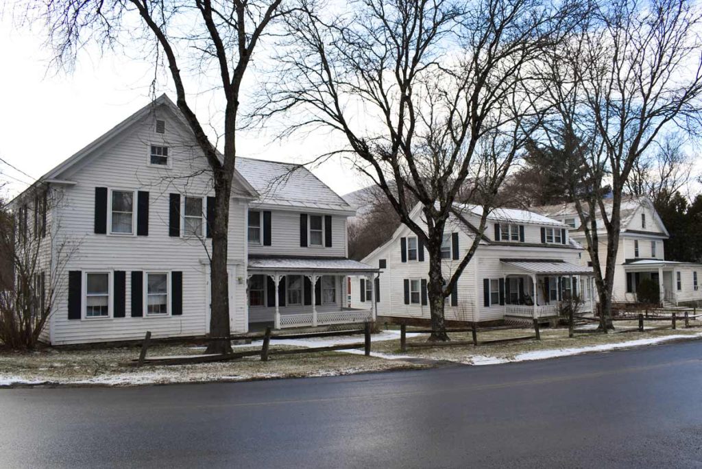 Exterior of white homes as viewed from the tree-lined street