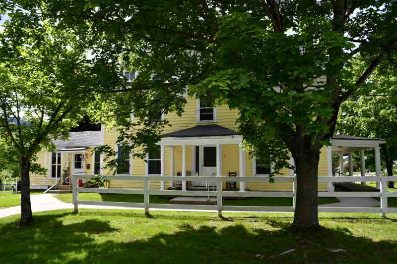 Yellow sprawling home converted to apartments on shady country road.