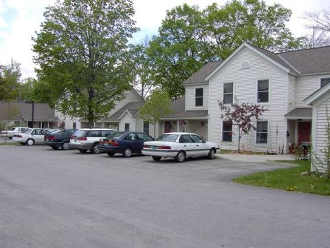 Image of a parking lot and apartment building surrounded by trees